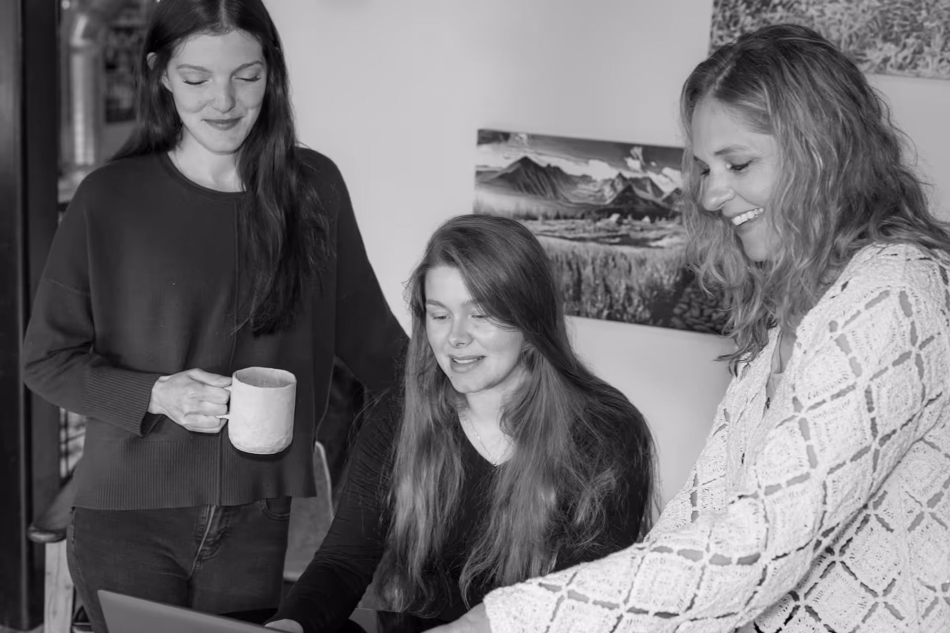 Three women collaborating happily around a laptop in a cozy indoor setting.